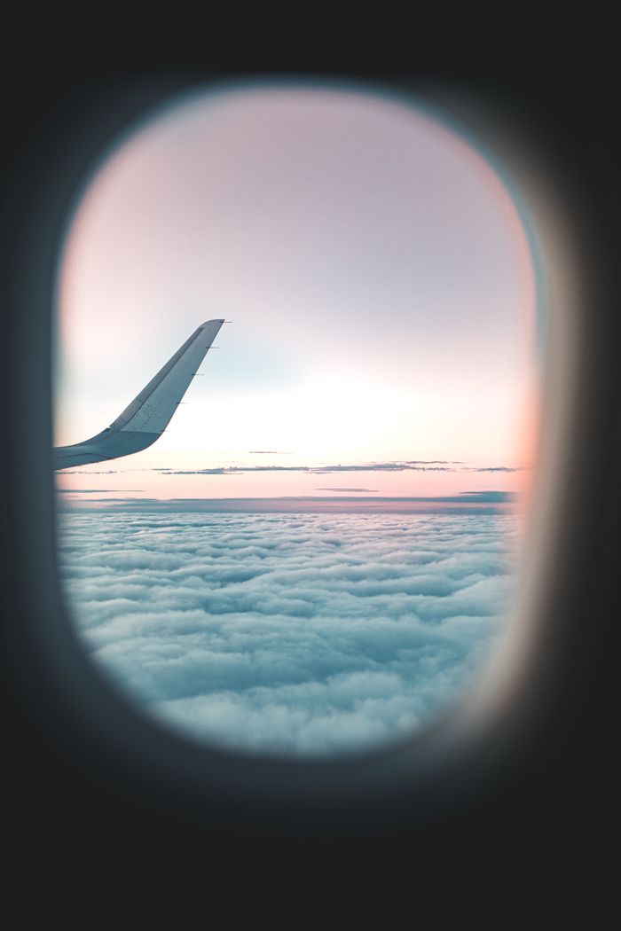 View from airplane window showing wing and clouds at sunset.