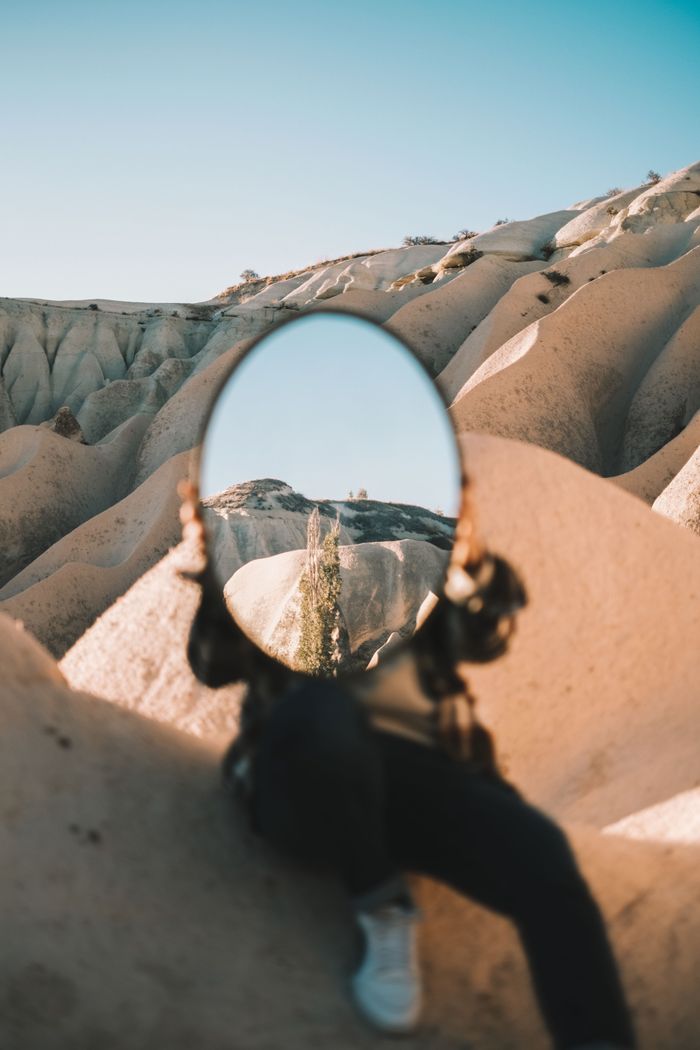 A person holds a mirror reflecting a Cappadocia landscape, beautifully capturing nature and art.