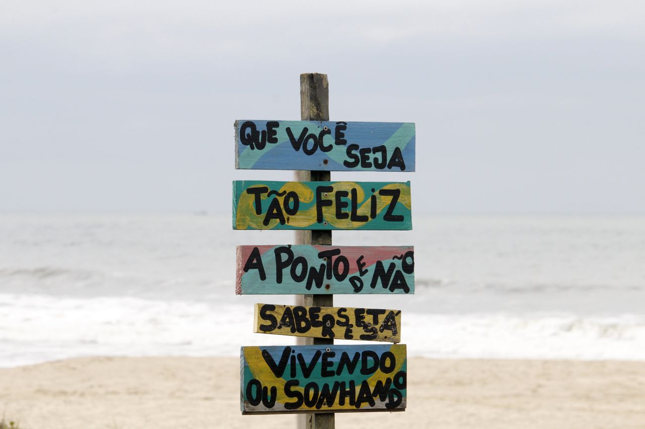 Colorful beach sign in Guaratuba, Brazil with motivational text against ocean waves.